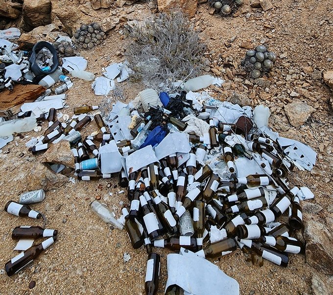 A pile of bottles, cans and other trash sits on a desert landscape