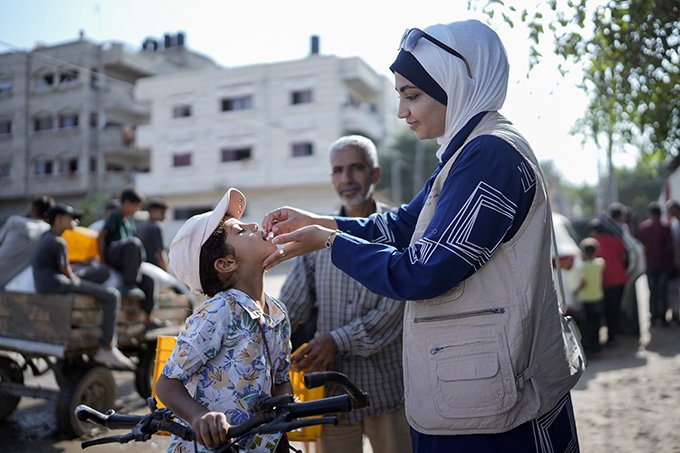 A woman administers an oral polio vaccine to a young boy.